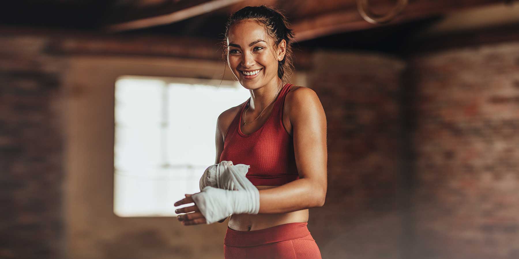 Jeune femme sourriante qui met ses bandages pour son premier cours de boxe