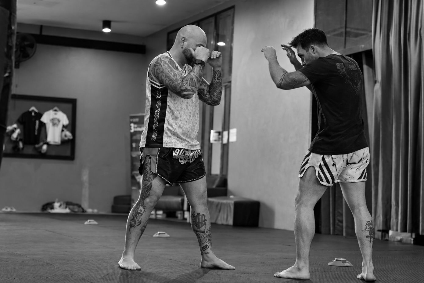Deux hommes en garde se font face dans une salle sobre, loin d’un ring